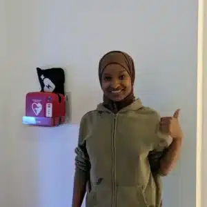 Smiling man in a hoodie giving thumbs up near wall-mounted AED.