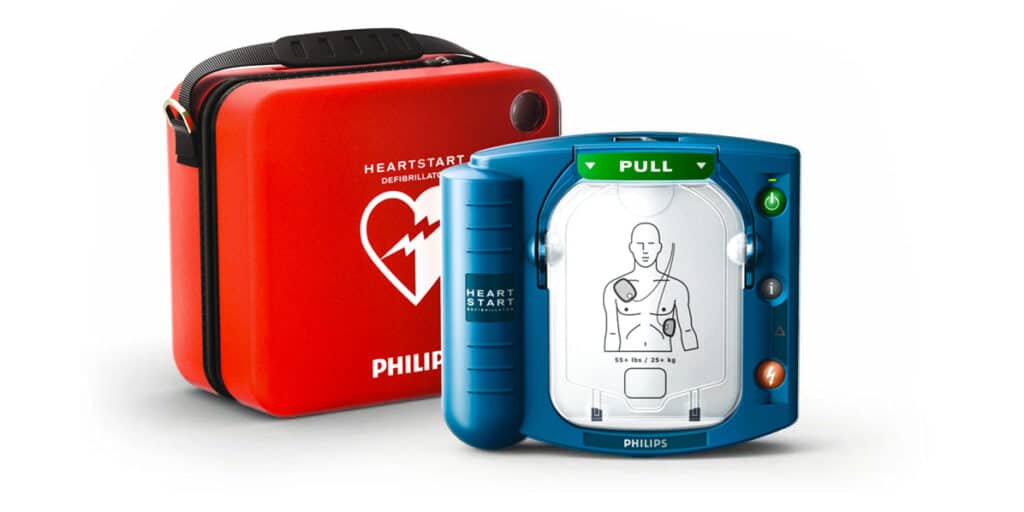 Philips HeartStart HS1 defibrillator with illustrated electrode pad and red carry case.