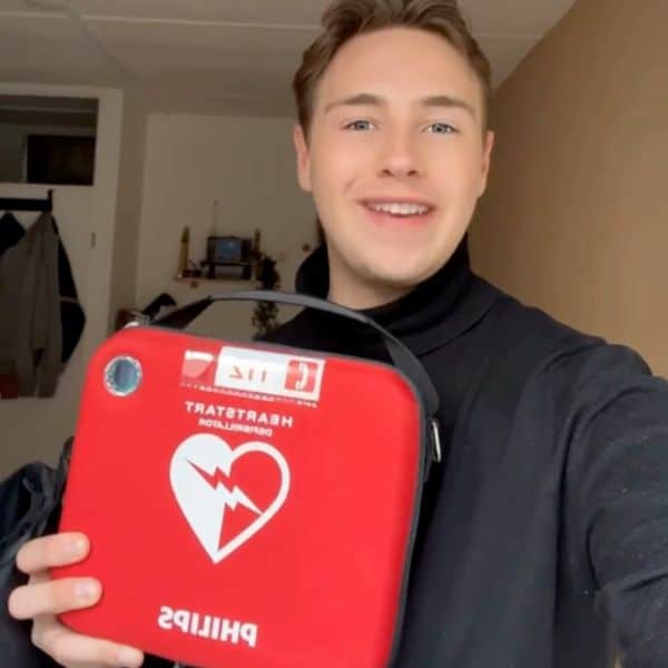 Young man holding a red defibrillator and smiling in a room with warm lighting.